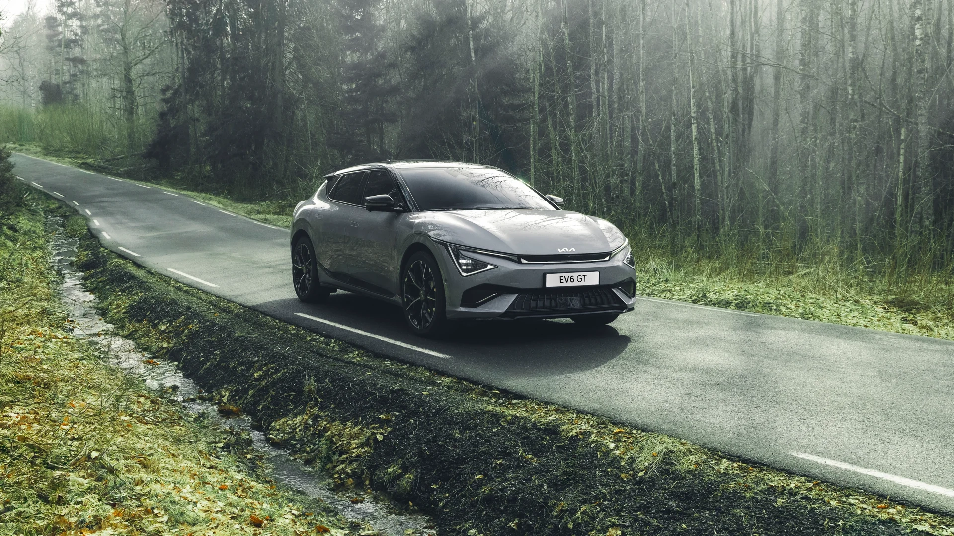 Kia EV6 GT i sølvgrå farge på landevei gjennom skog – elektrisk ytelsesbil hos Granrud Bilverksted.