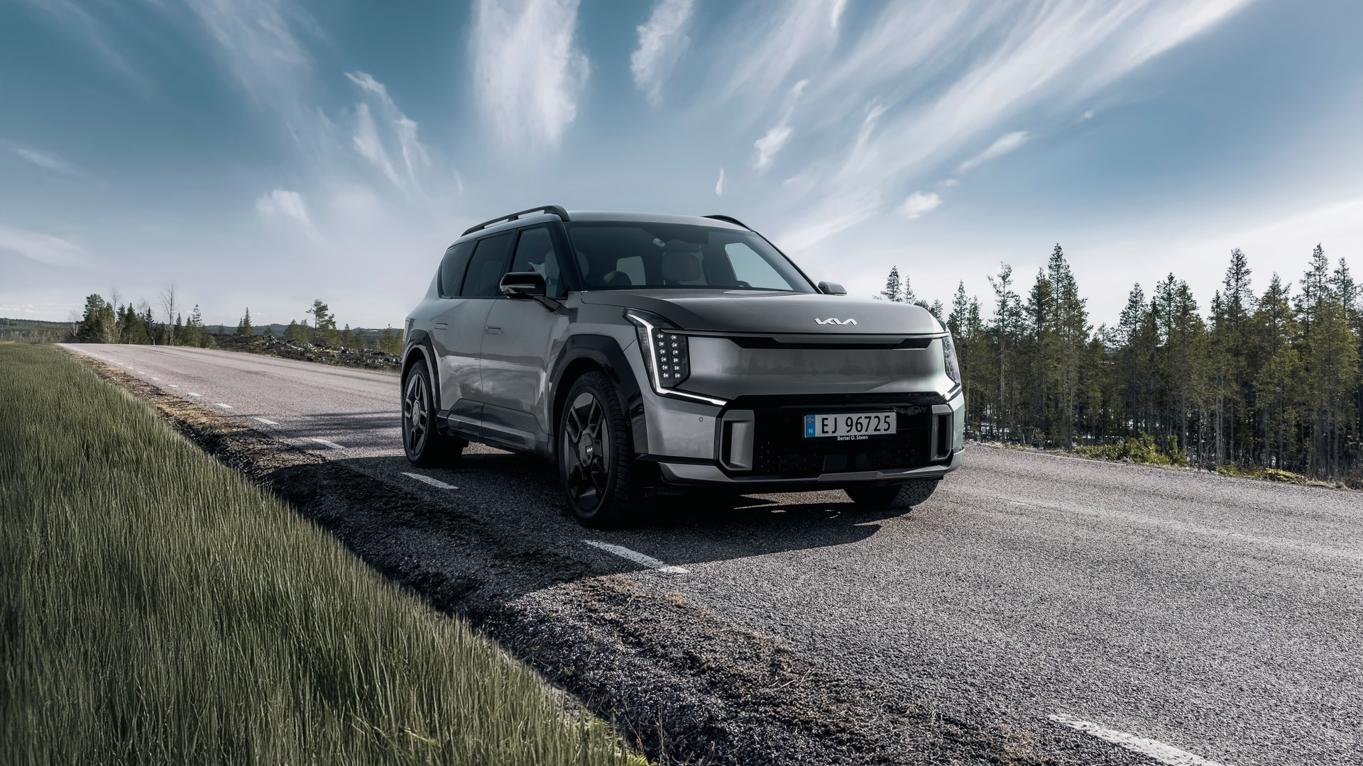 Kia EV9 i sølvgrå finish kjører på landevei under blå himmel – elektrisk familie-SUV fra Granrud Bilverksted.