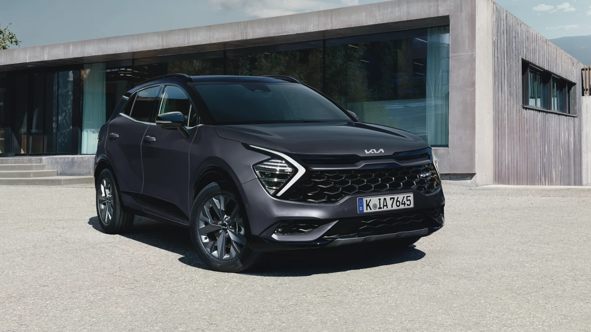 Kia Sportage i mørk lakkert finish foran moderne arkitektur – kompakt og praktisk SUV hos Granrud Bilverksted.